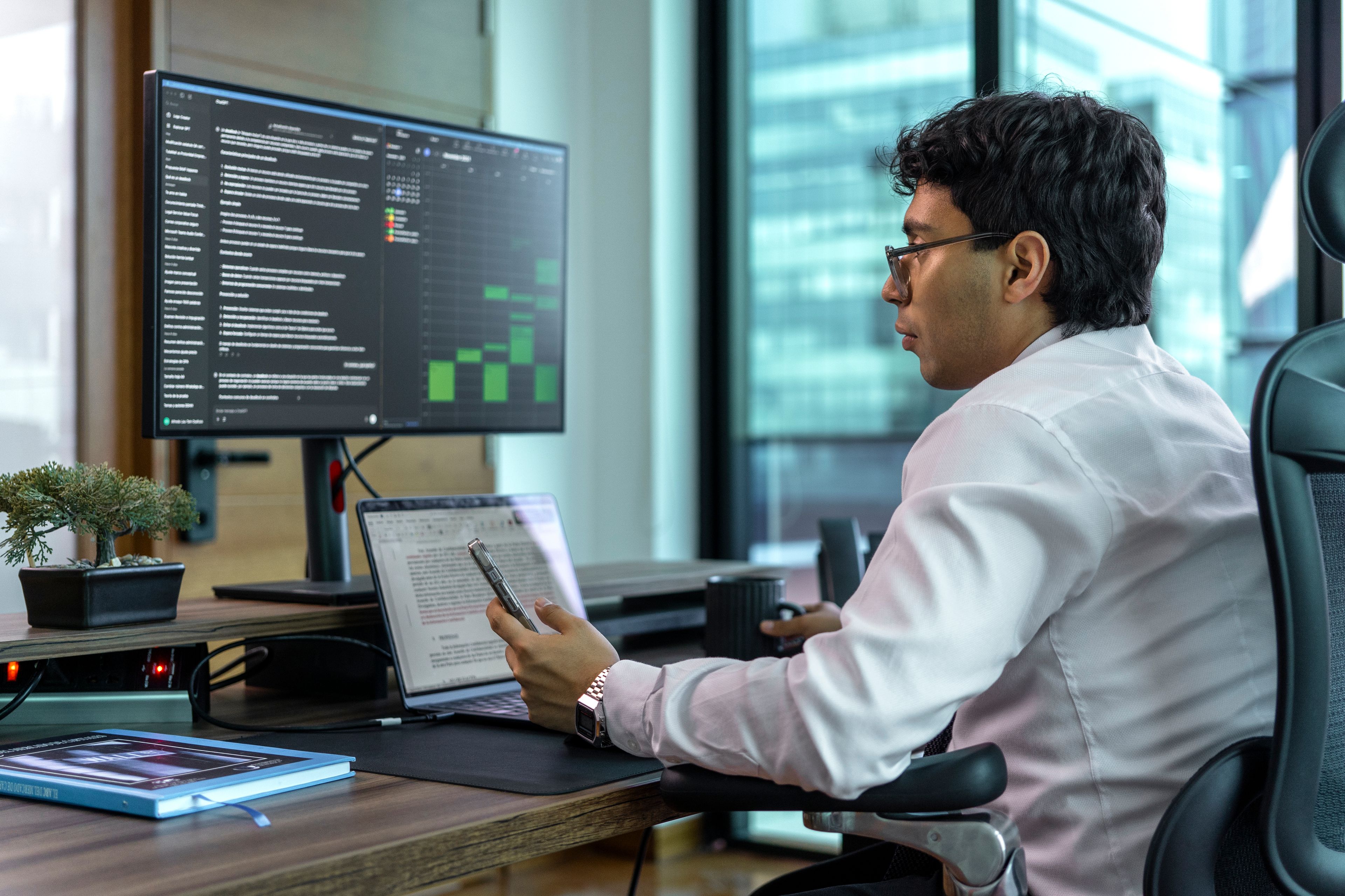 Profissional analisando informações em um monitor e uma planilha no notebook em um escritório
